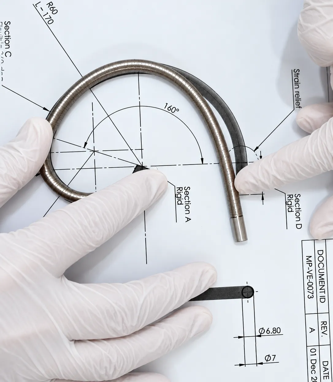 Hands holding a reinforced shaft with rigid and flexible sections over its engineering drawing